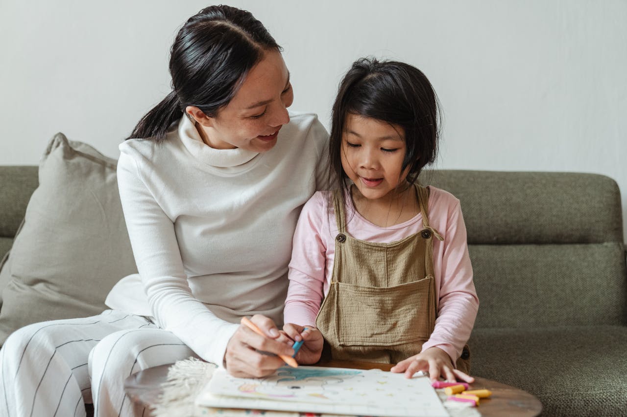 A mother helps her young daughter with a colorful drawing at home, fostering creativity and bonding.